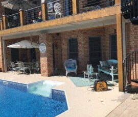 A backyard pool area with patio furniture, a staircase, and upper and lower covered seating areas at a brick house.