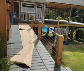 Gray deck with wooden railing, a rolled-up piece of paper or material on the walkway, and a house in the background.