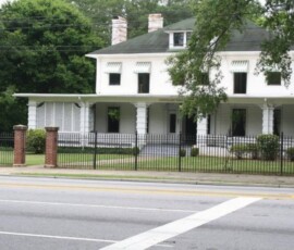 Large white two-story house with green awnings, a front porch, and a black iron fence along the sidewalk.