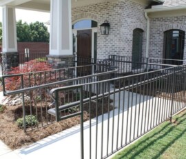 An accessible wheelchair ramp with black railings leads to the entrance of a brick building with landscaping nearby.
