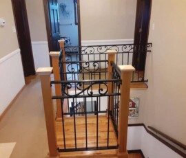 A staircase landing with decorative black metal railings and wooden posts blocking access to the hallway.
